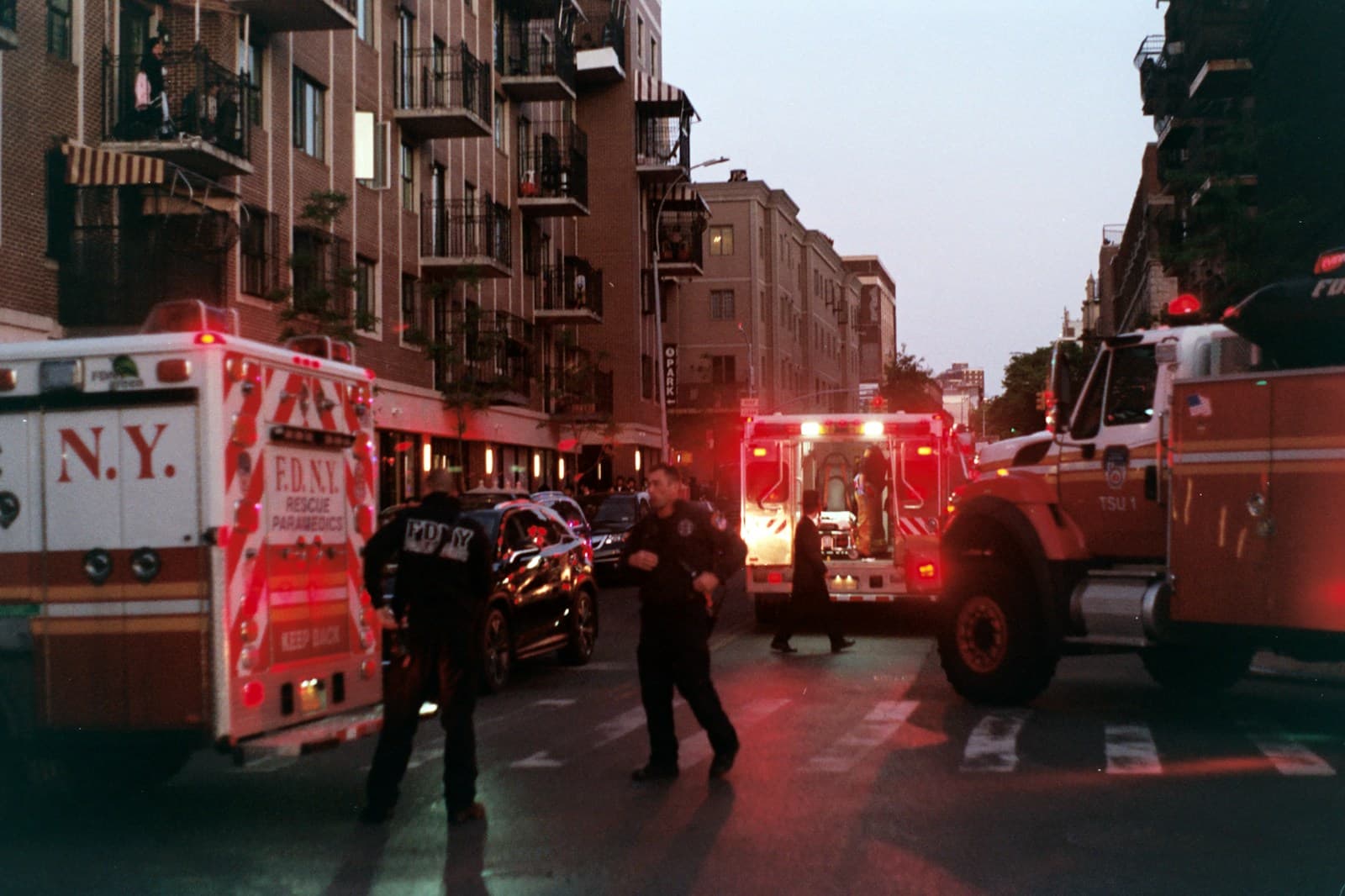 Fire trucks and emergency vehicles with red flashing lights responding to an incident on a city street at dusk