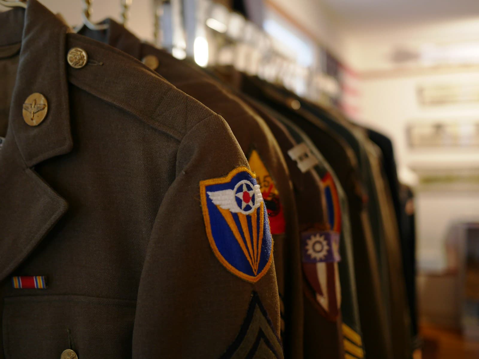 Row of military uniforms hanging on a rack, the nearest showing a unit patch