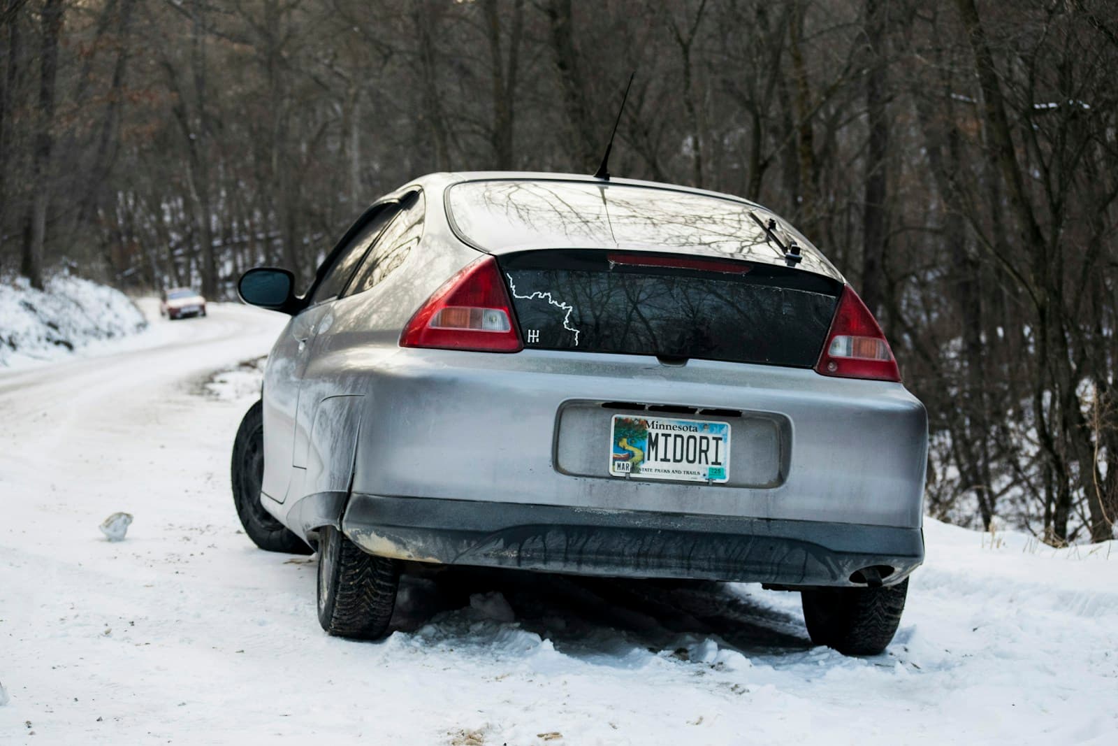 Silver sedan stuck at an angle in deep snow on a wooded rural road in winter