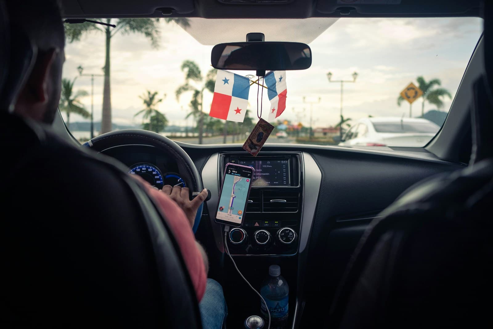 Interior view of a driver at the wheel with a mounted phone, tropical scenery ahead