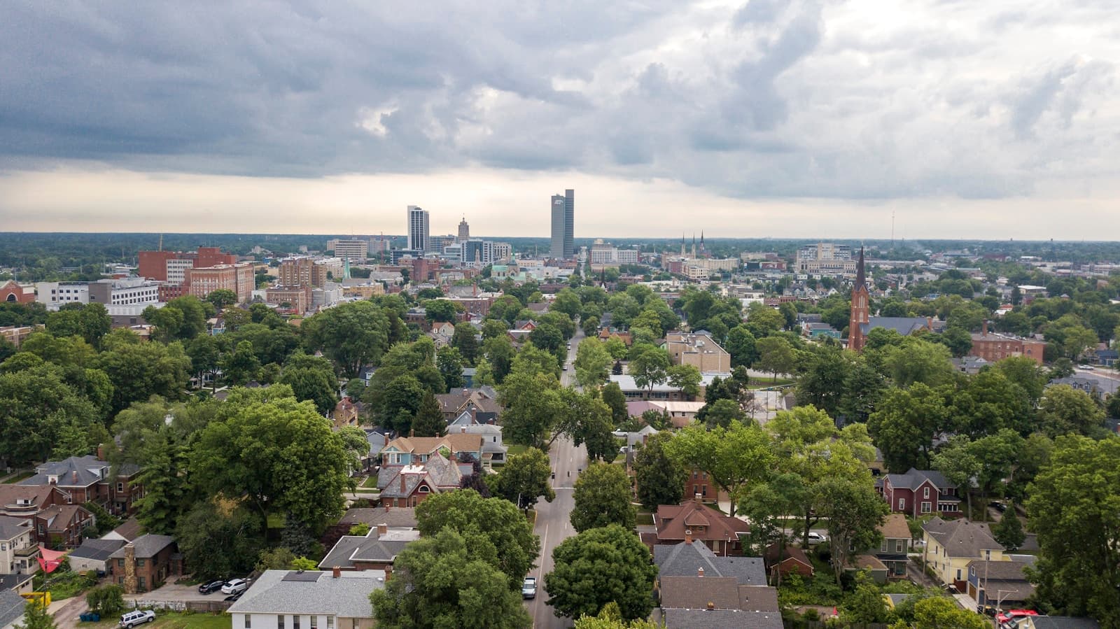 Aerial view of residential neighborhood with trees leading to downtown city skyline under cloudy sky
