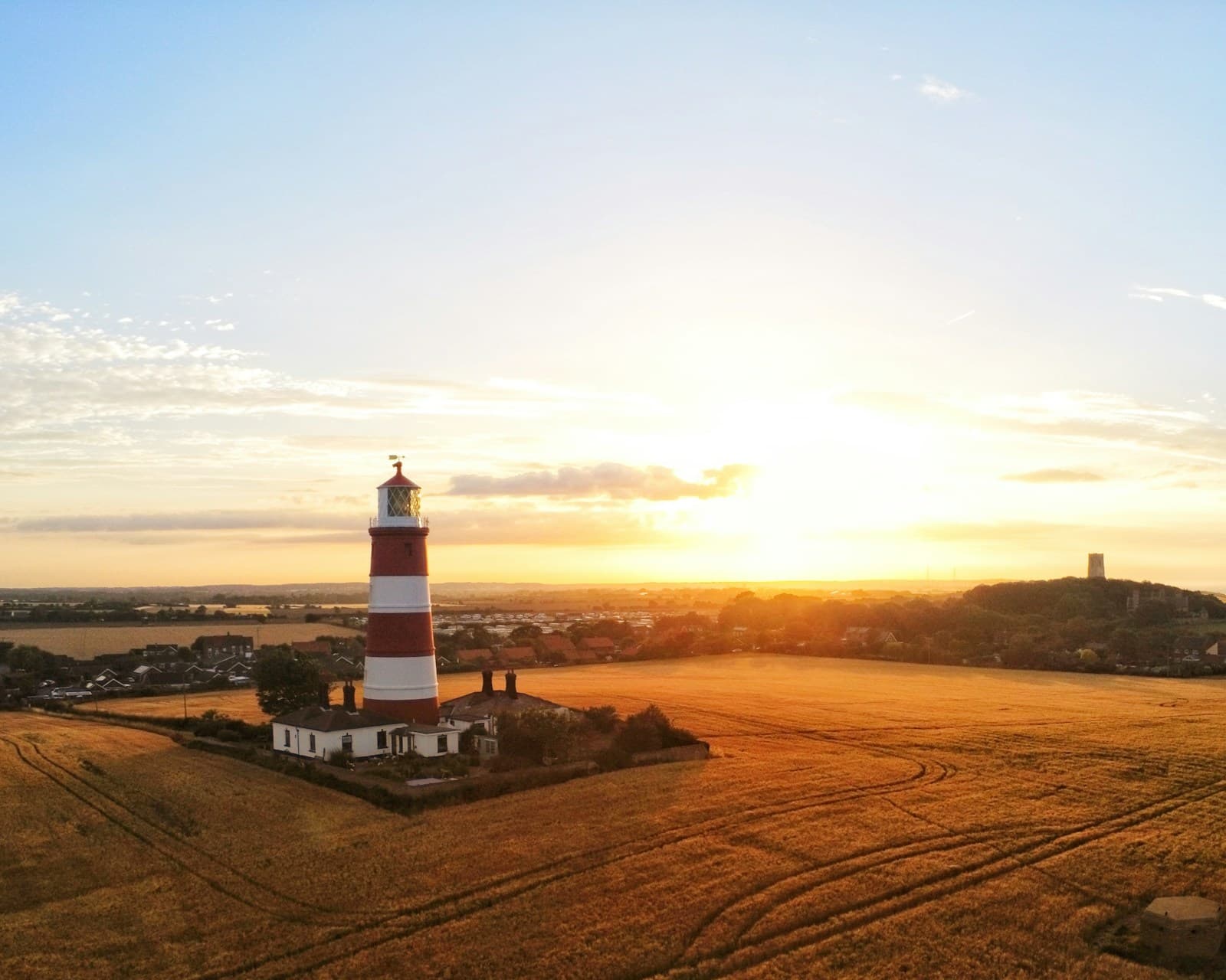 Red and white striped lighthouse on golden farmland at sunset with rolling fields and curved plow lines