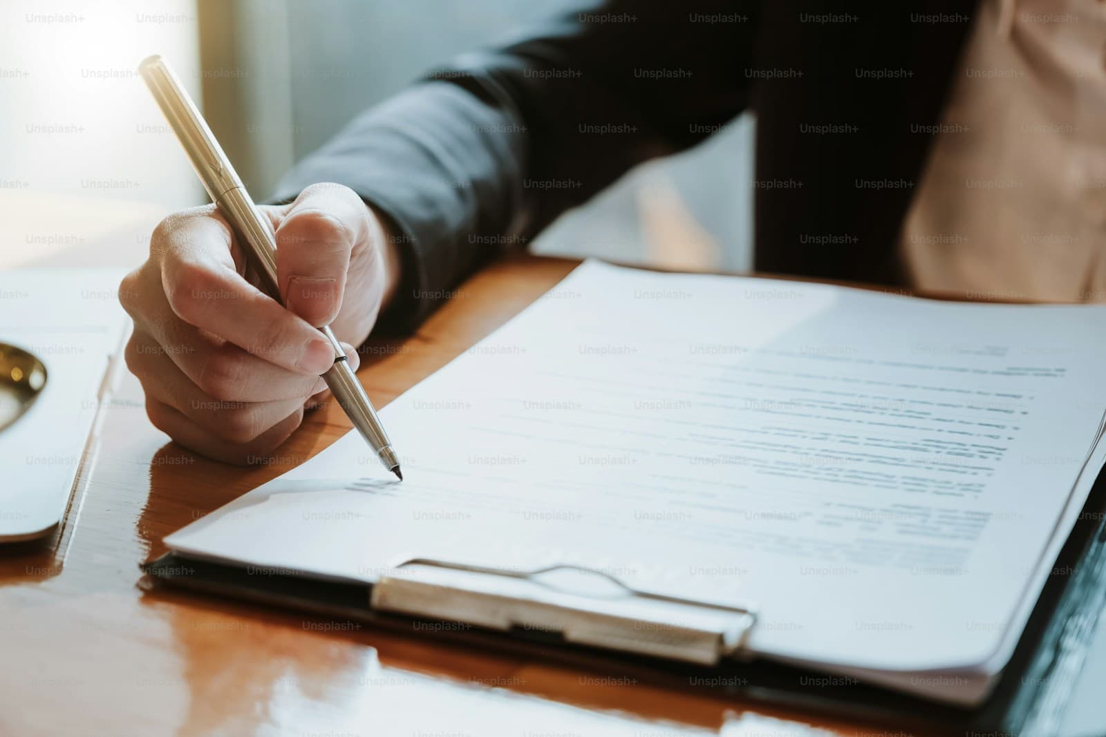 Professional woman writing with pen on business documents at wooden desk