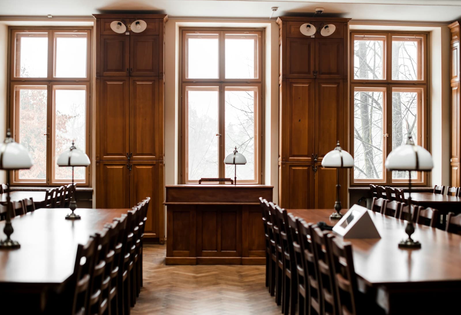 Traditional library reading room with wooden tables, black chairs, and tall windows