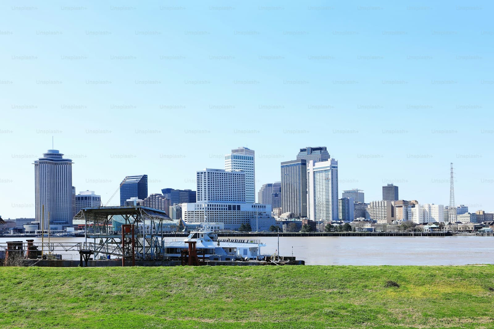 City skyline with tall buildings viewed across water from grassy waterfront area on clear day
