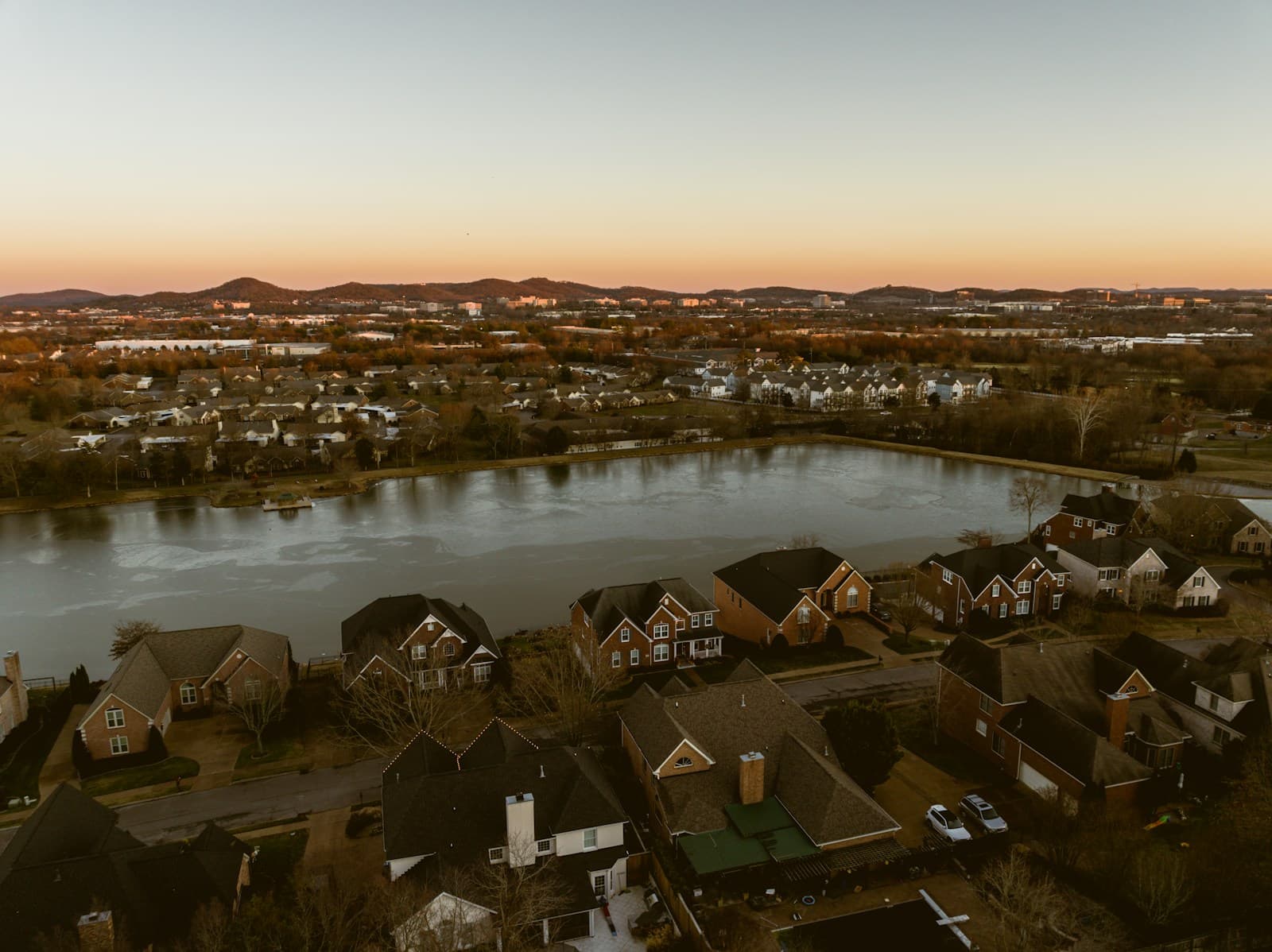 Aerial view of upscale lakeside suburban neighborhood at sunset with large homes around a lake