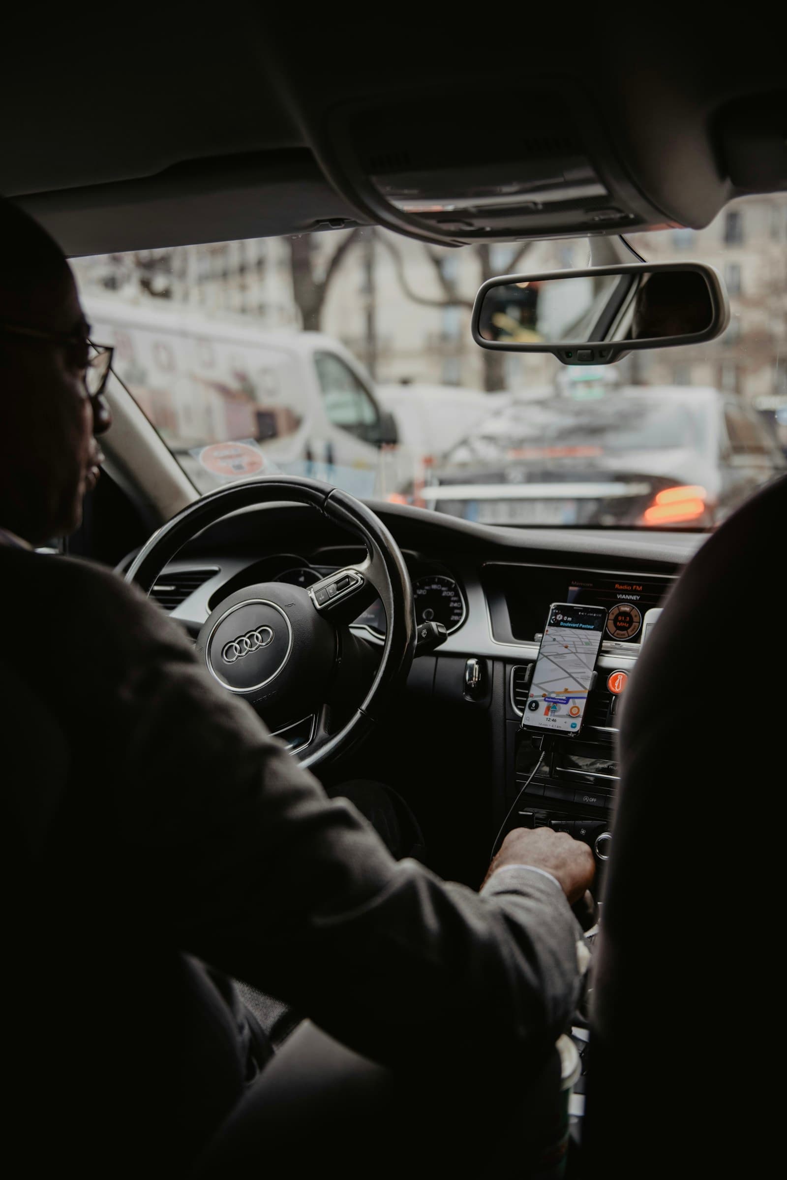 Driver in an Audi checking a smartphone while parked on an urban street
