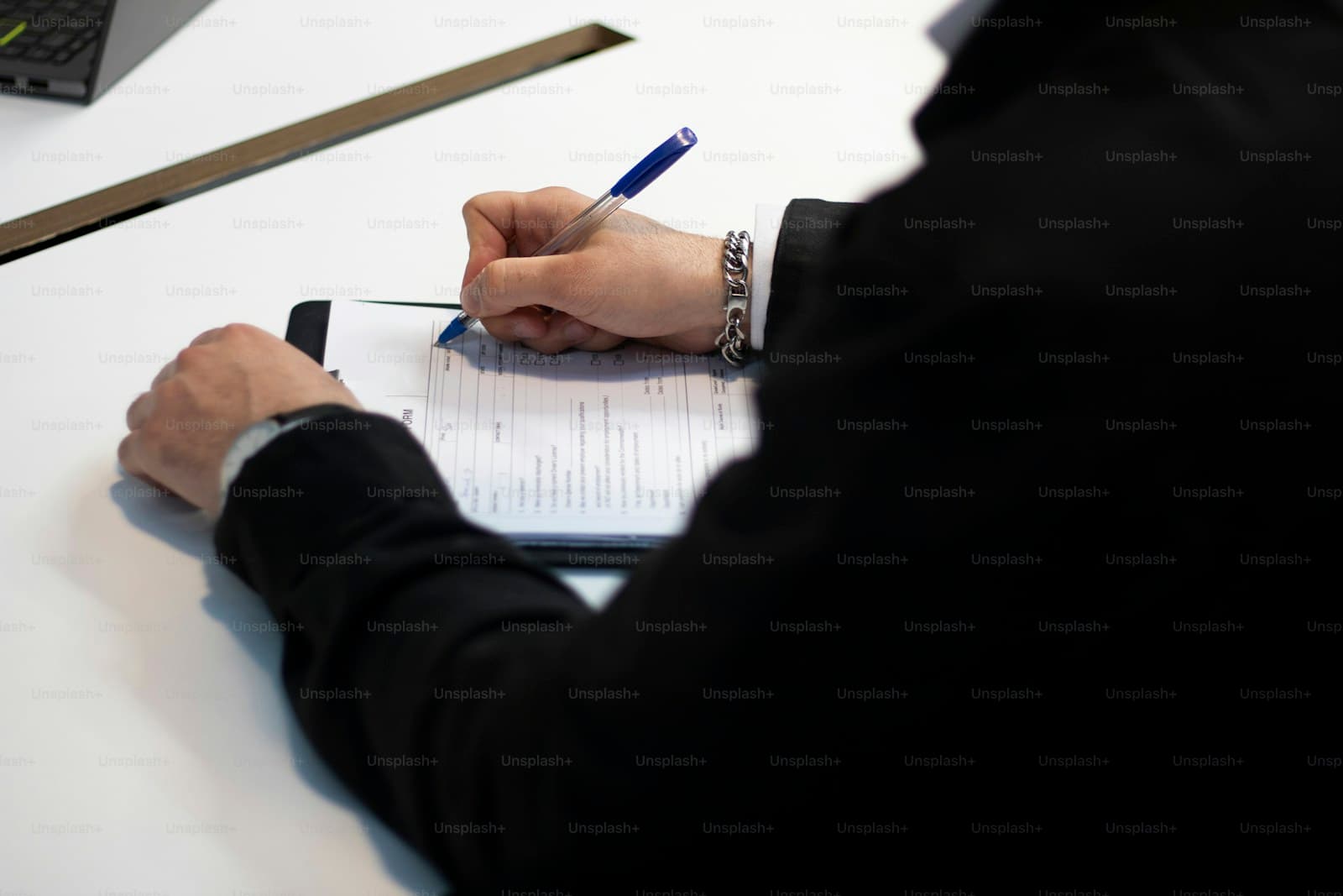 Person in dark clothing writing on white paper with blue pen at desk
