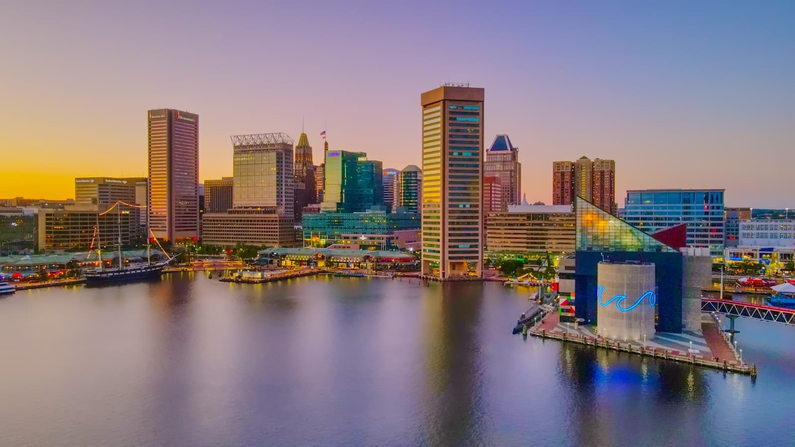 Baltimore Inner Harbor skyline at sunset with skyscrapers reflected in calm water under colorful evening sky