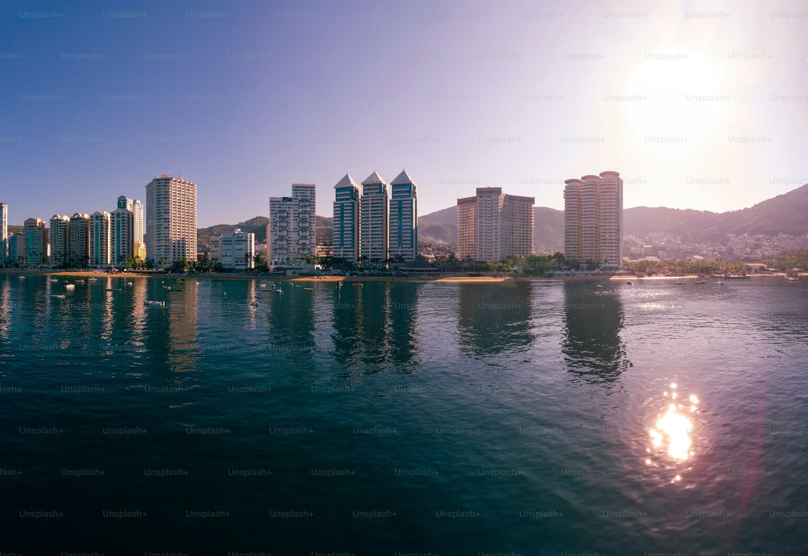 City skyline reflected in water at sunset with golden light and purple-orange sky