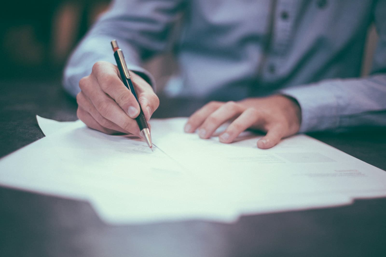 Person in a dress shirt writing on white paperwork at a desk
