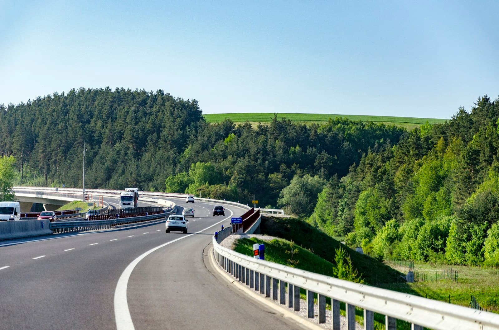Highway curving through green forested hills with cars and trucks driving on multi-lane road