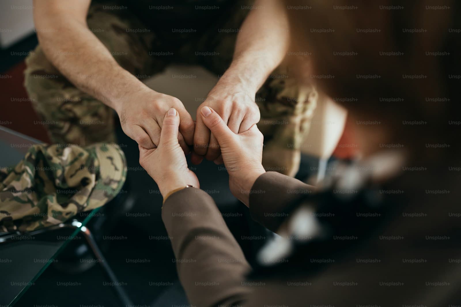 Two people sitting close and holding hands, one in camouflage trousers