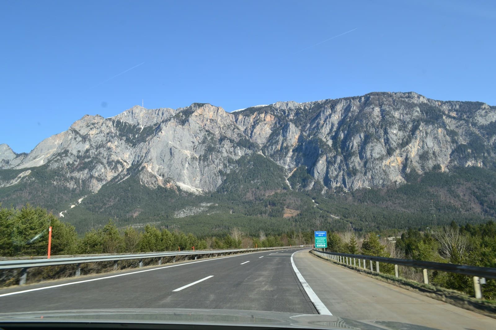 Curved guardrailed highway leading toward limestone mountains under clear blue sky