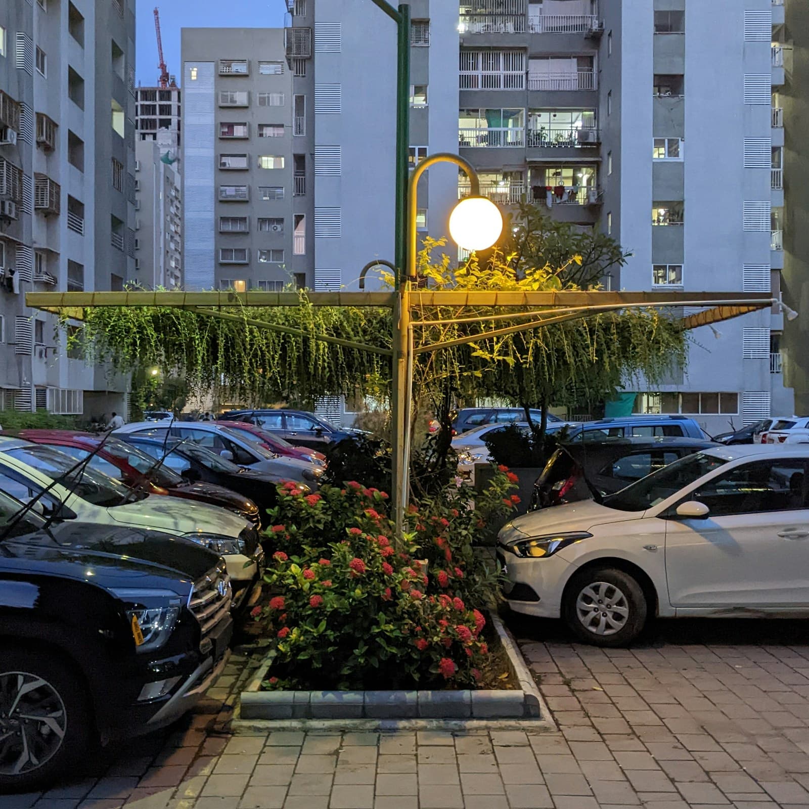 Evening view of apartment complex parking area with illuminated street lamp and landscaped garden bed