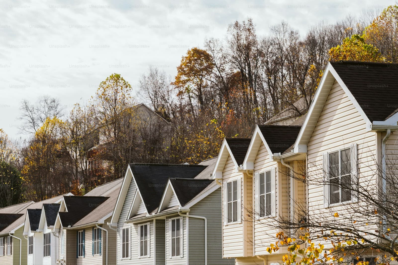 Row of white and beige townhouses with autumn trees on hillside in background