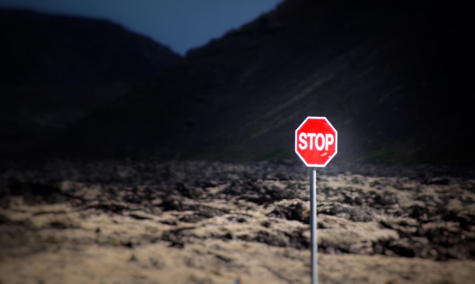 Red stop sign standing alone in desert landscape with mountains in background at dusk