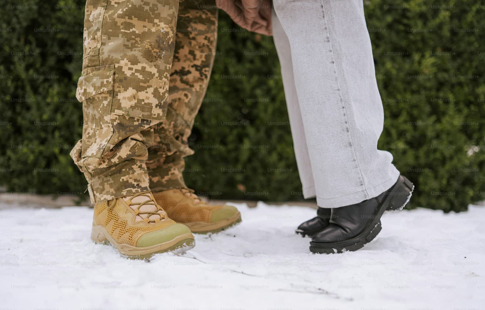 Two people standing in snow, one in camouflage trousers and tan combat boots