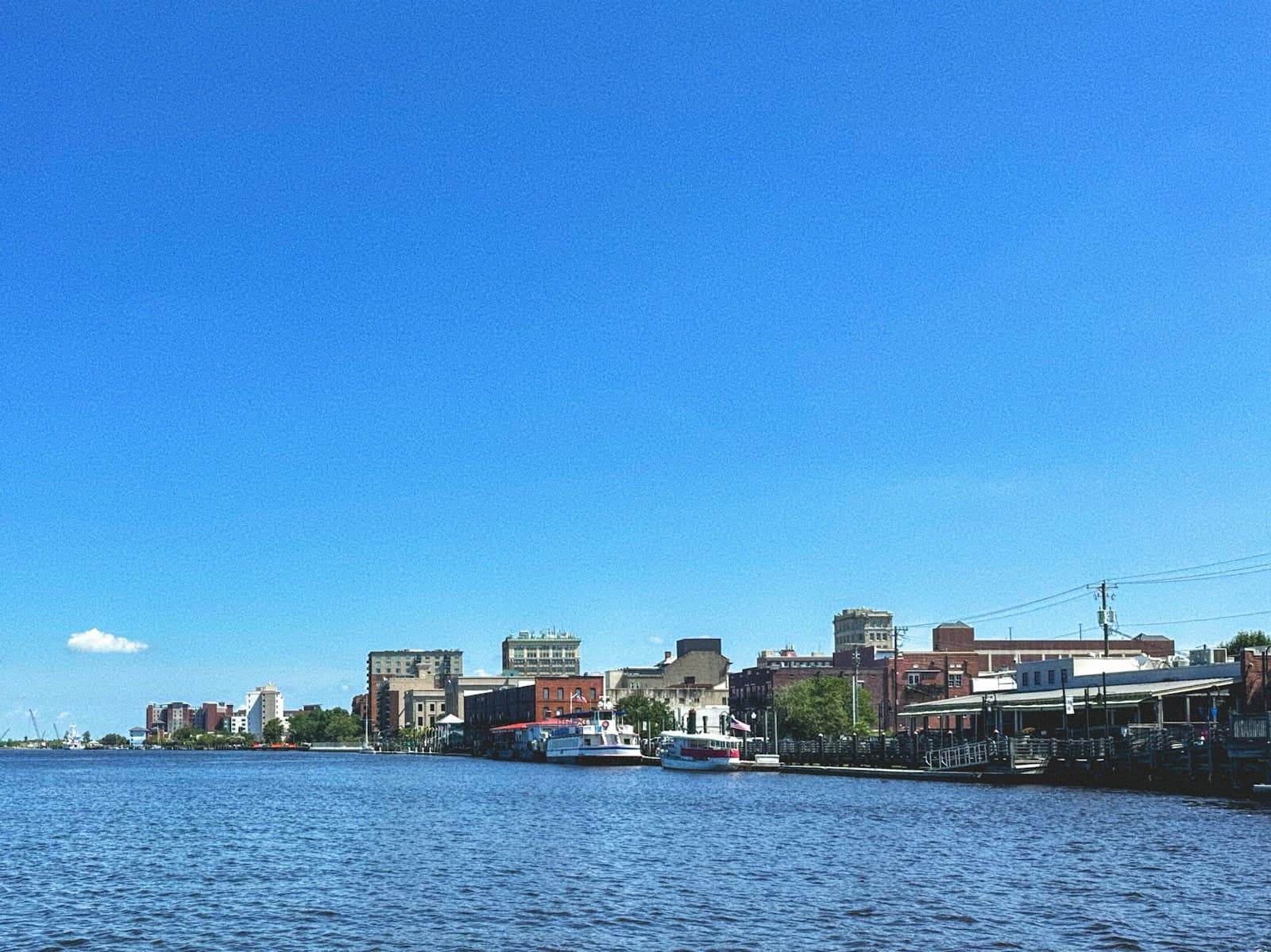 City waterfront skyline with buildings along the shore under clear blue sky, viewed across calm water