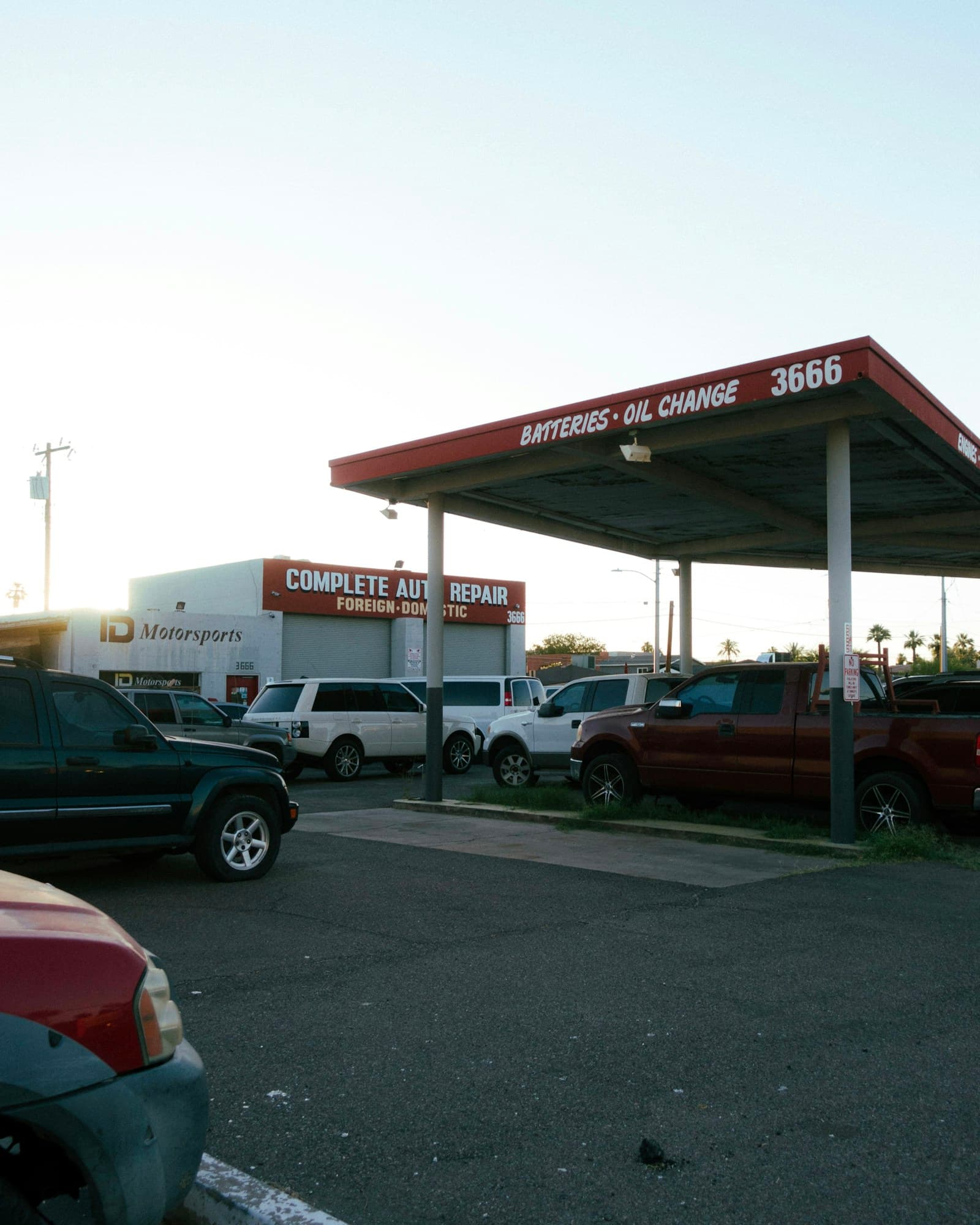 Gas station and auto repair shop with cars parked beneath the fuel canopy at dusk
