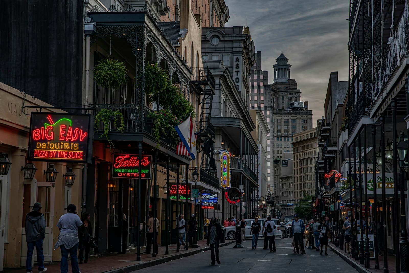 Evening street scene in New Orleans French Quarter with historic buildings, neon signs, and pedestrians walking