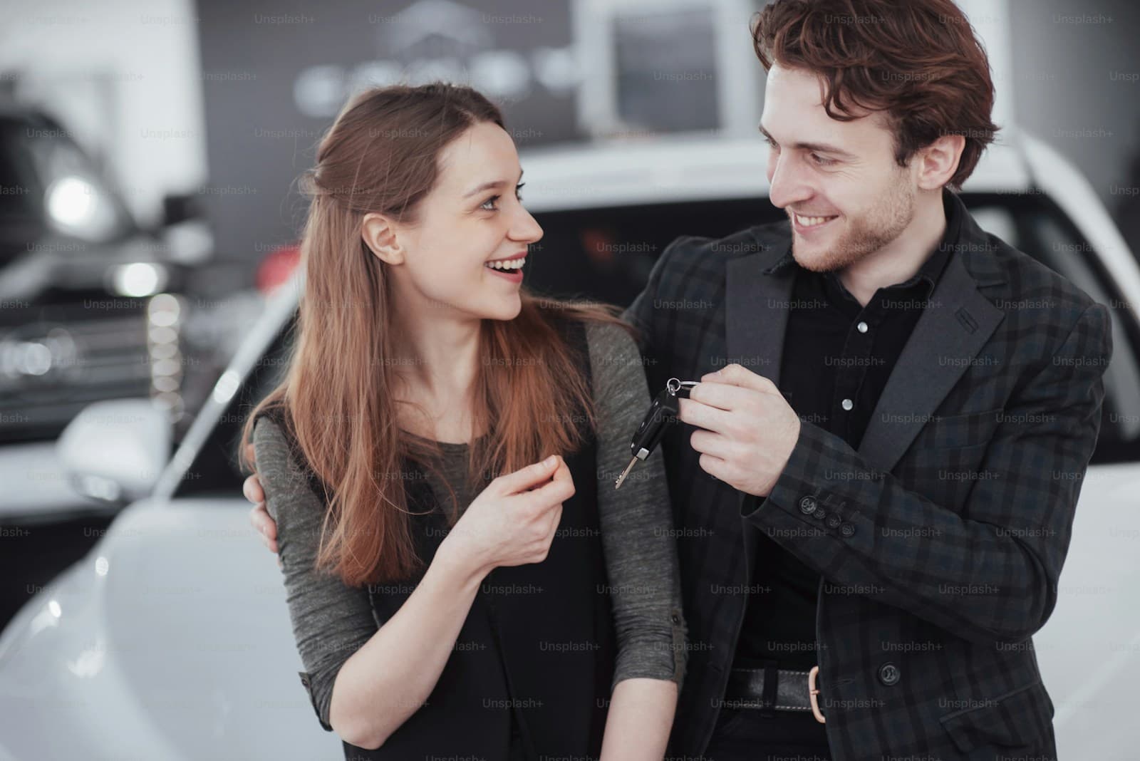 Young couple smiling in a dealership showroom, the man holding a new set of car keys