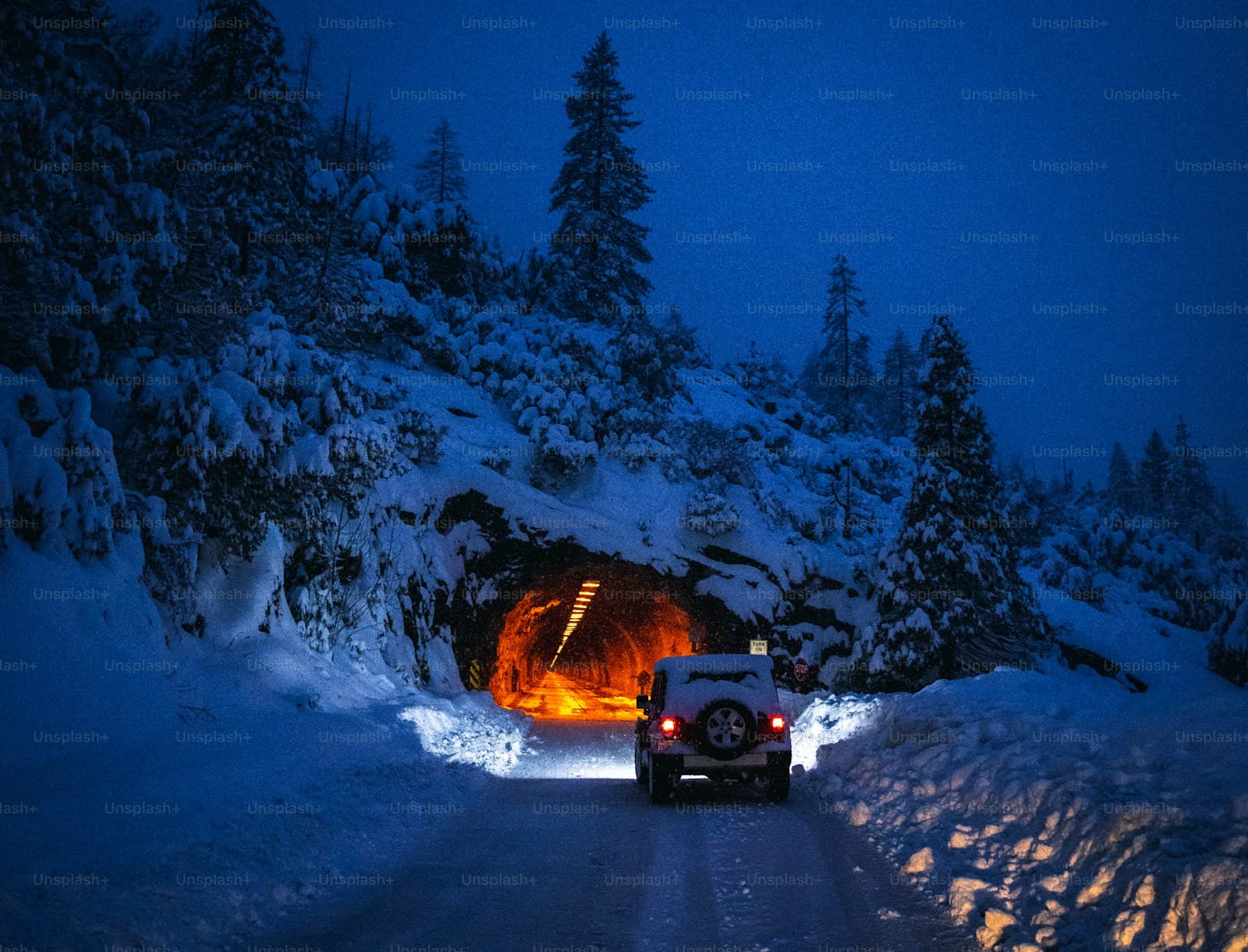 SUV driving through snow tunnel at twilight with evergreen trees and deep blue sky