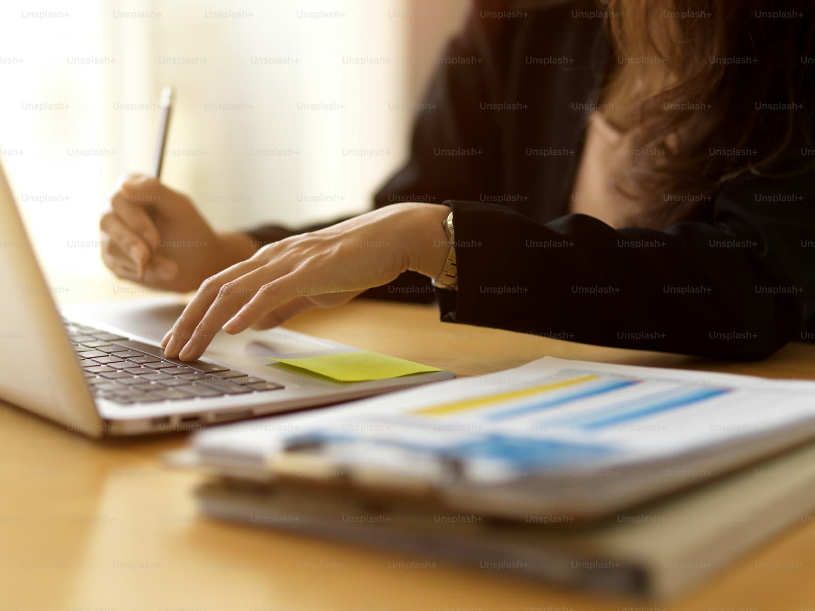 Woman working on laptop with business charts and documents on wooden desk