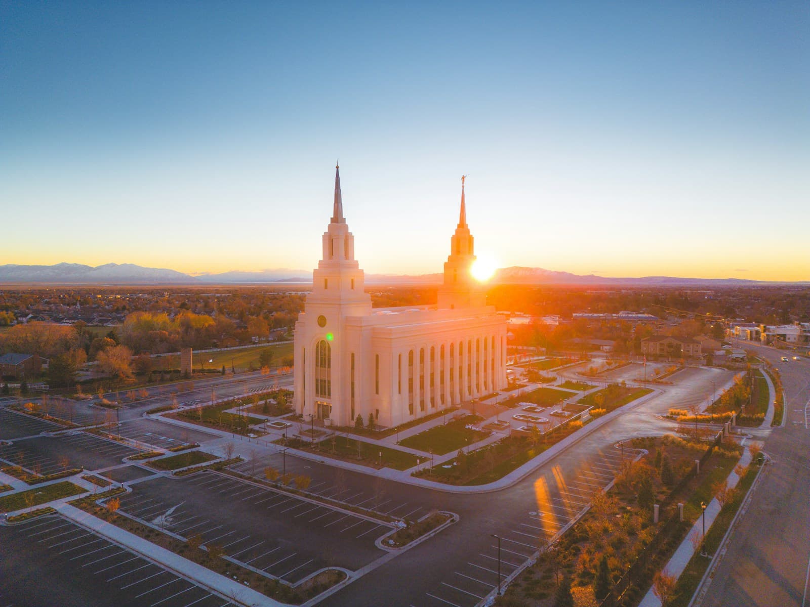 Aerial view of white Mormon temple with twin spires at sunset, surrounded by parking lots and residential area