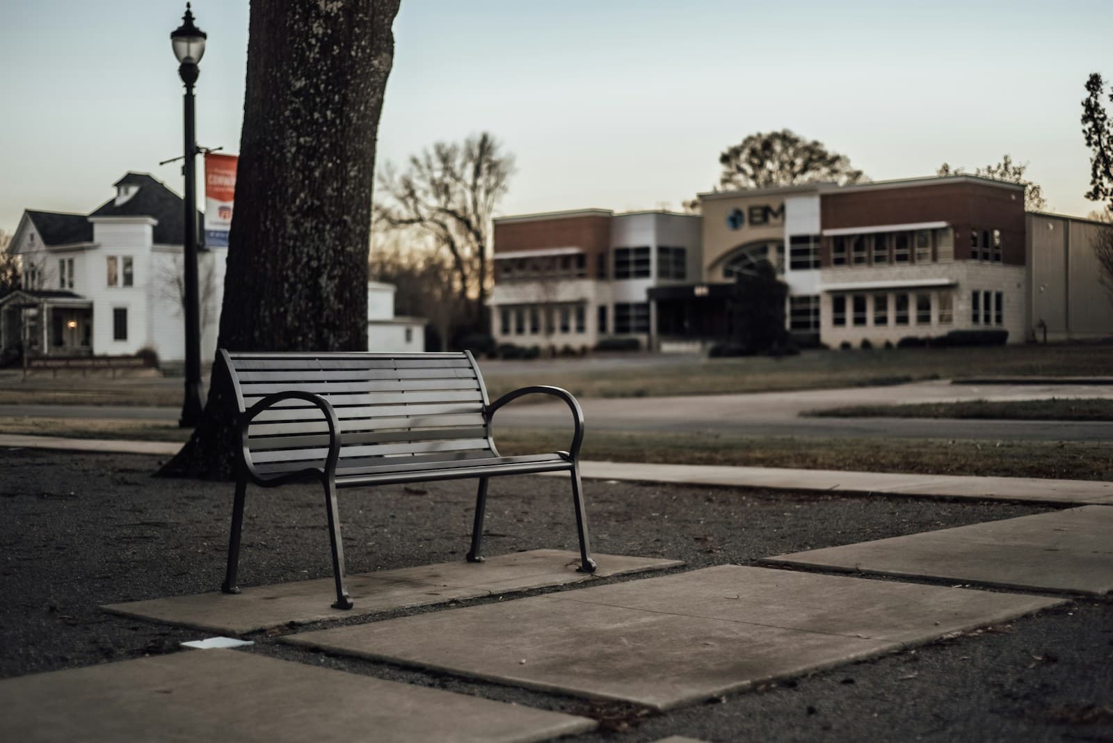 Empty park bench beside tree and street lamp in small town square with historic buildings in background