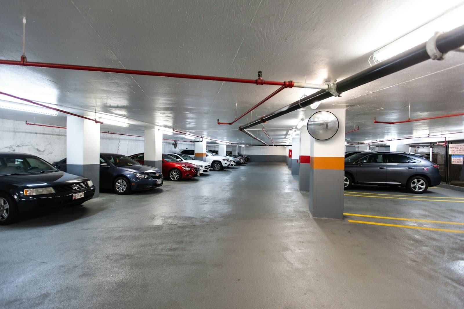 Underground parking garage with cars parked in spaces, concrete floors, and industrial lighting