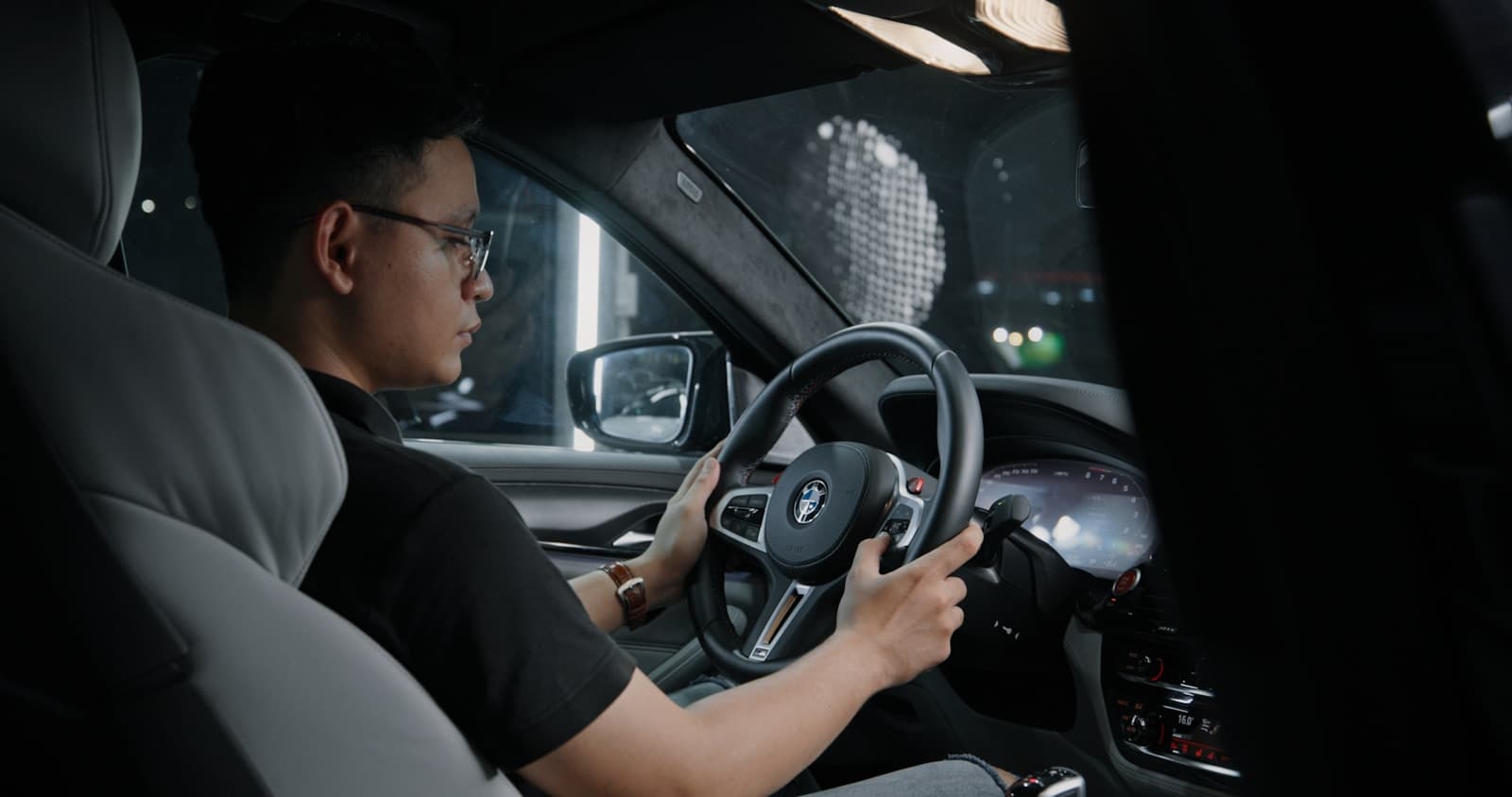 Man in glasses driving at night with the dashboard glowing in the dark