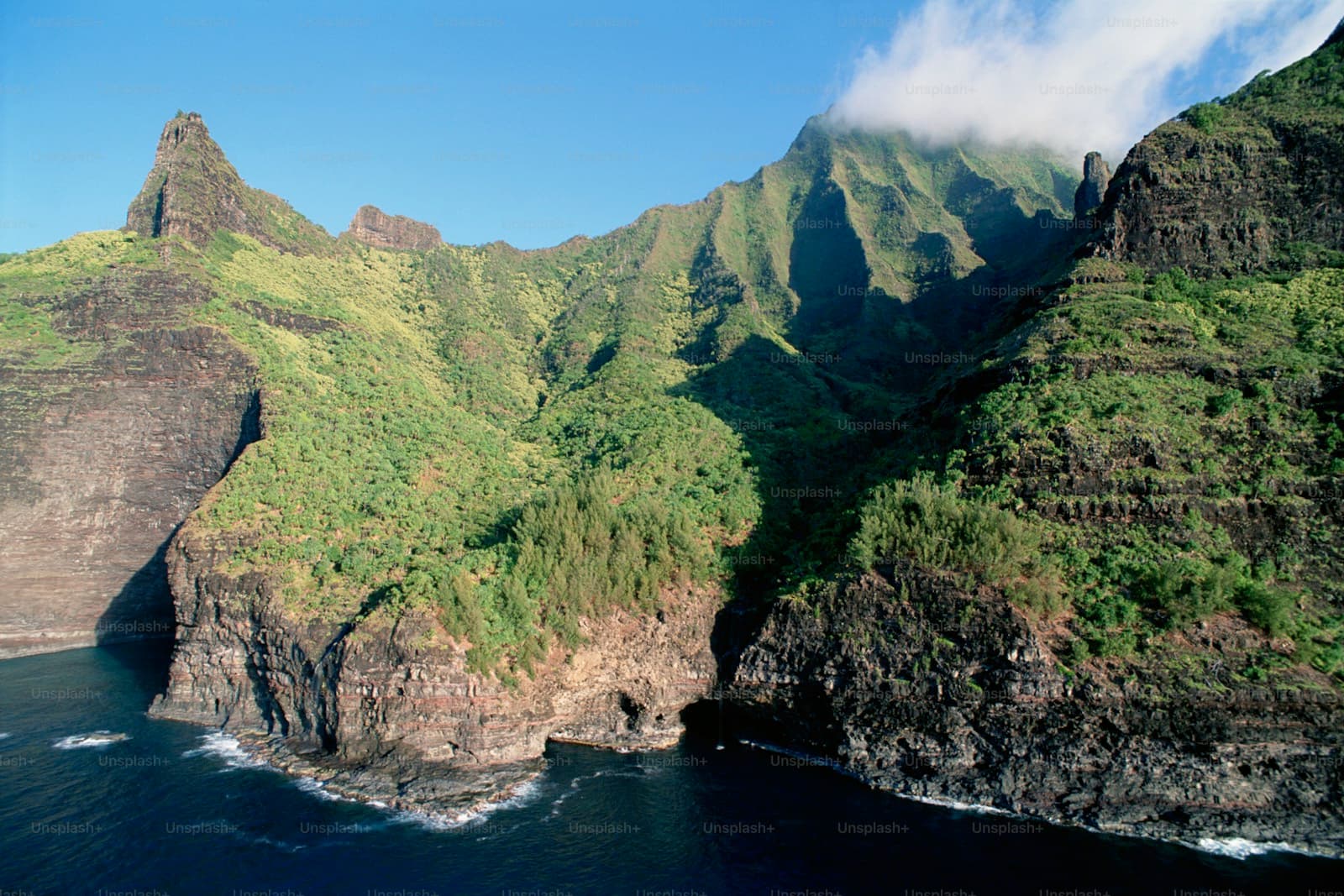 Aerial view of lush green coastal cliffs and volcanic ridges meeting the ocean under blue sky