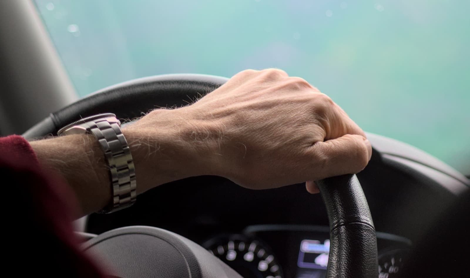 Hand with a metal watch band on the steering wheel, hazy light through the windshield