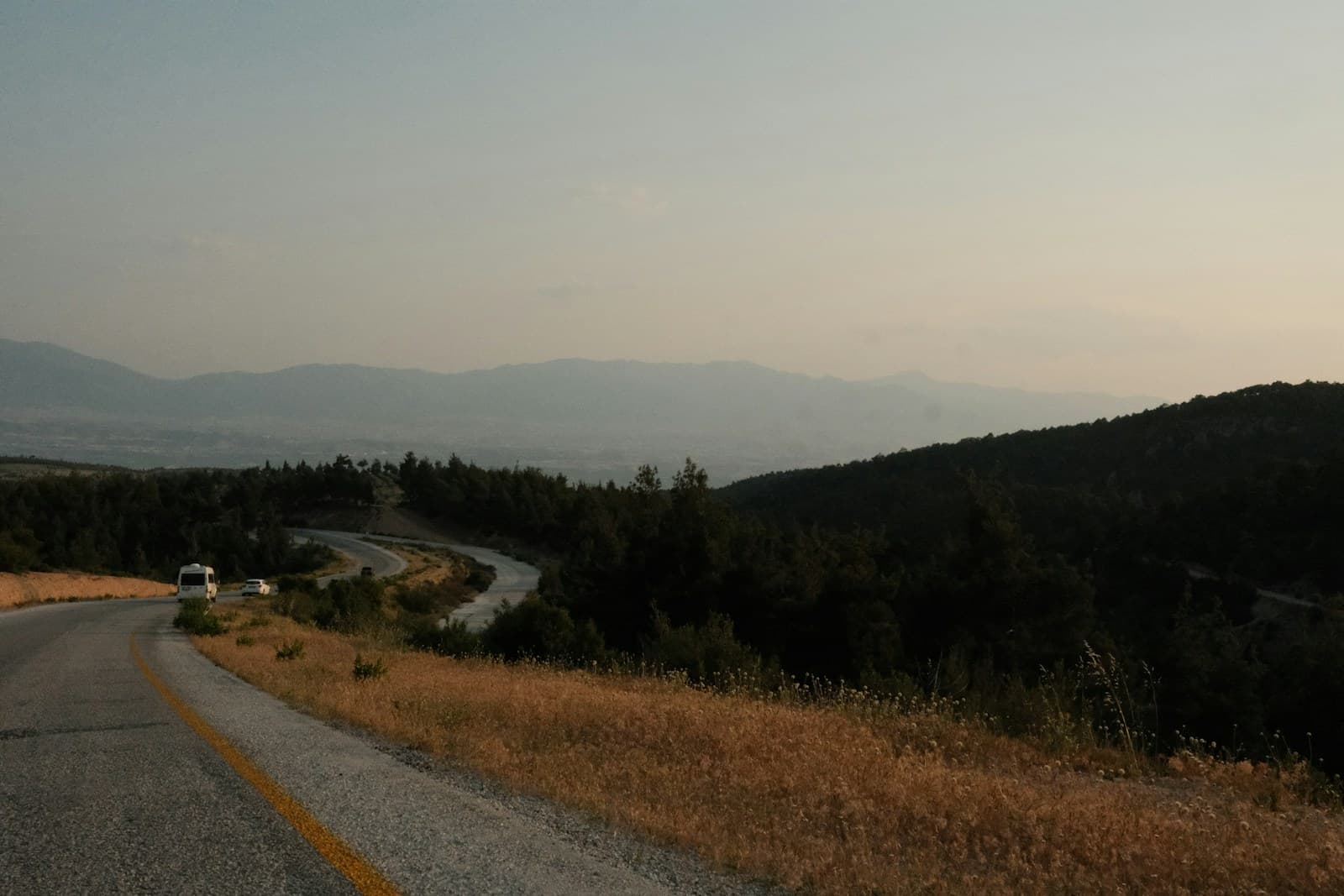 Winding rural road through hilly forest with hazy mountains in the distance