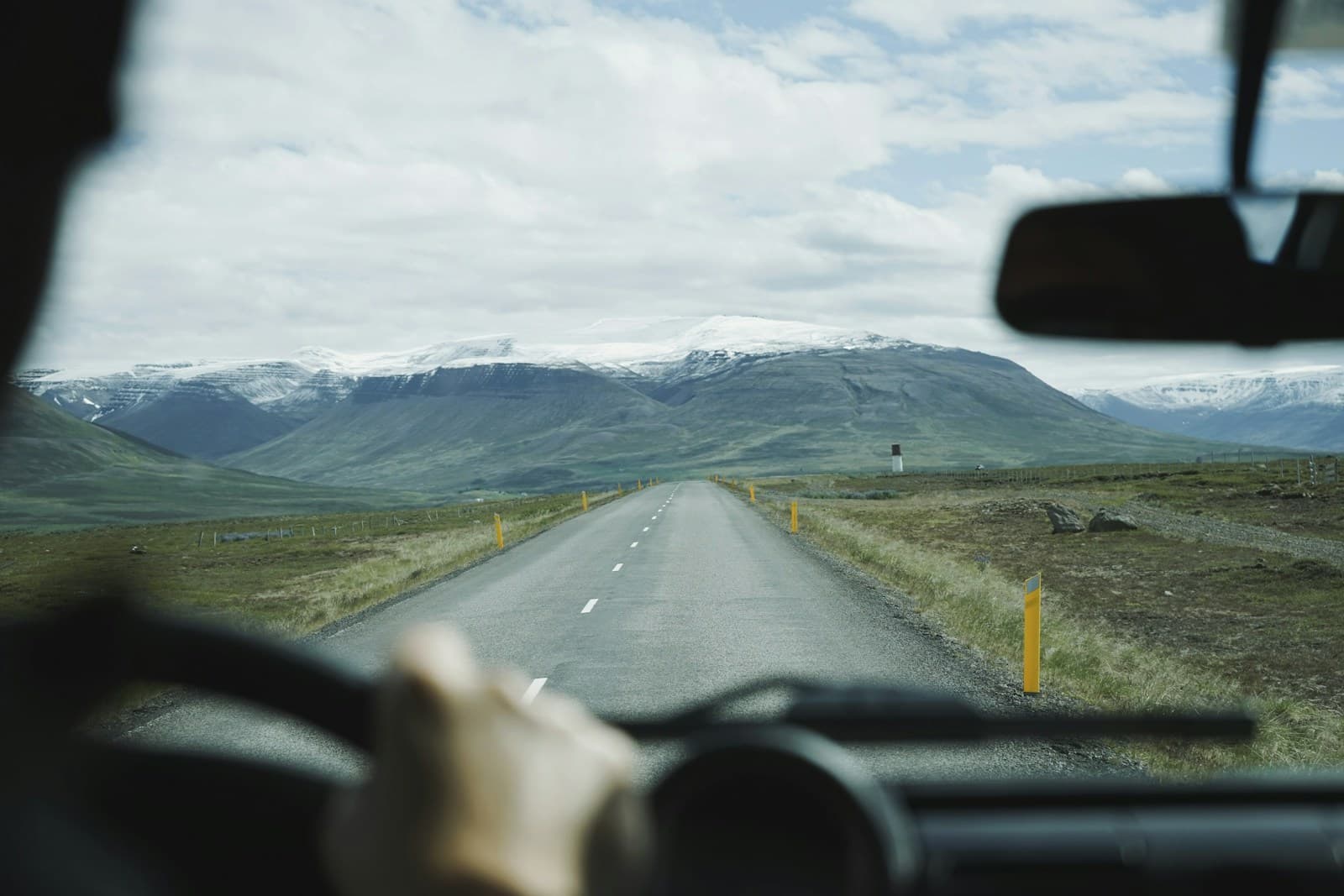 Driver on a two-lane road crossing a vast landscape toward snow-capped mountains