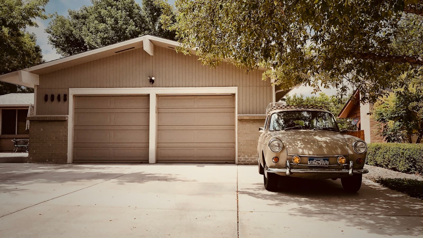 Vintage Volkswagen Beetle parked in front of a two-car garage in a suburban driveway