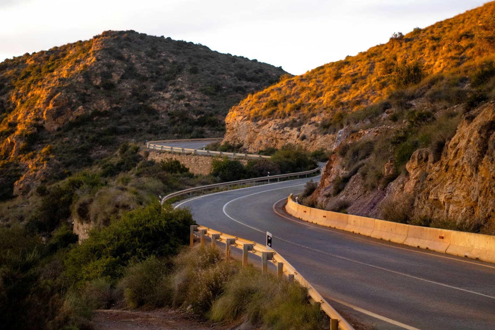 Winding guardrailed road through rolling hills lit by golden-hour sun