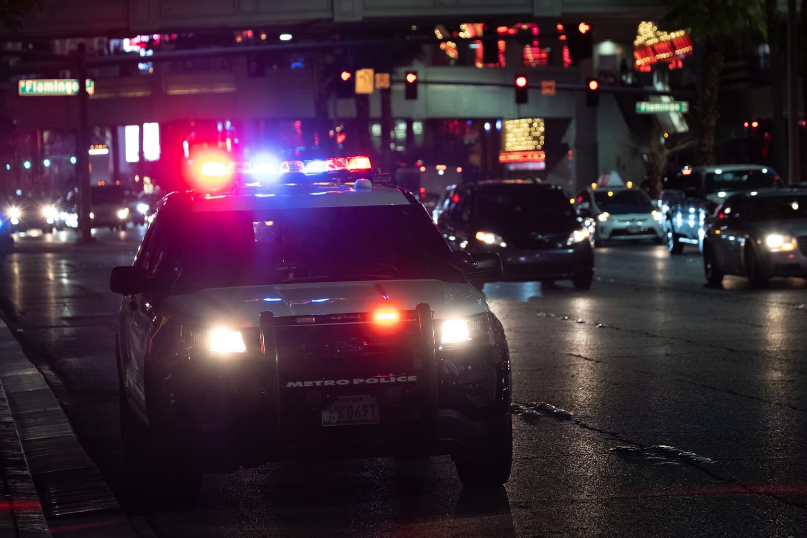 Police car with emergency lights activated on wet city street at night with neon signs in background