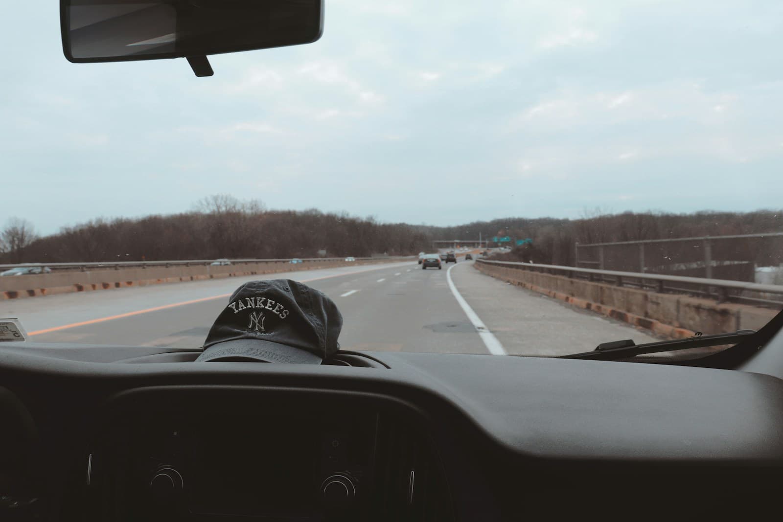 Interior car view of highway driving with dashboard visible, showing road ahead with trees and cloudy sky
