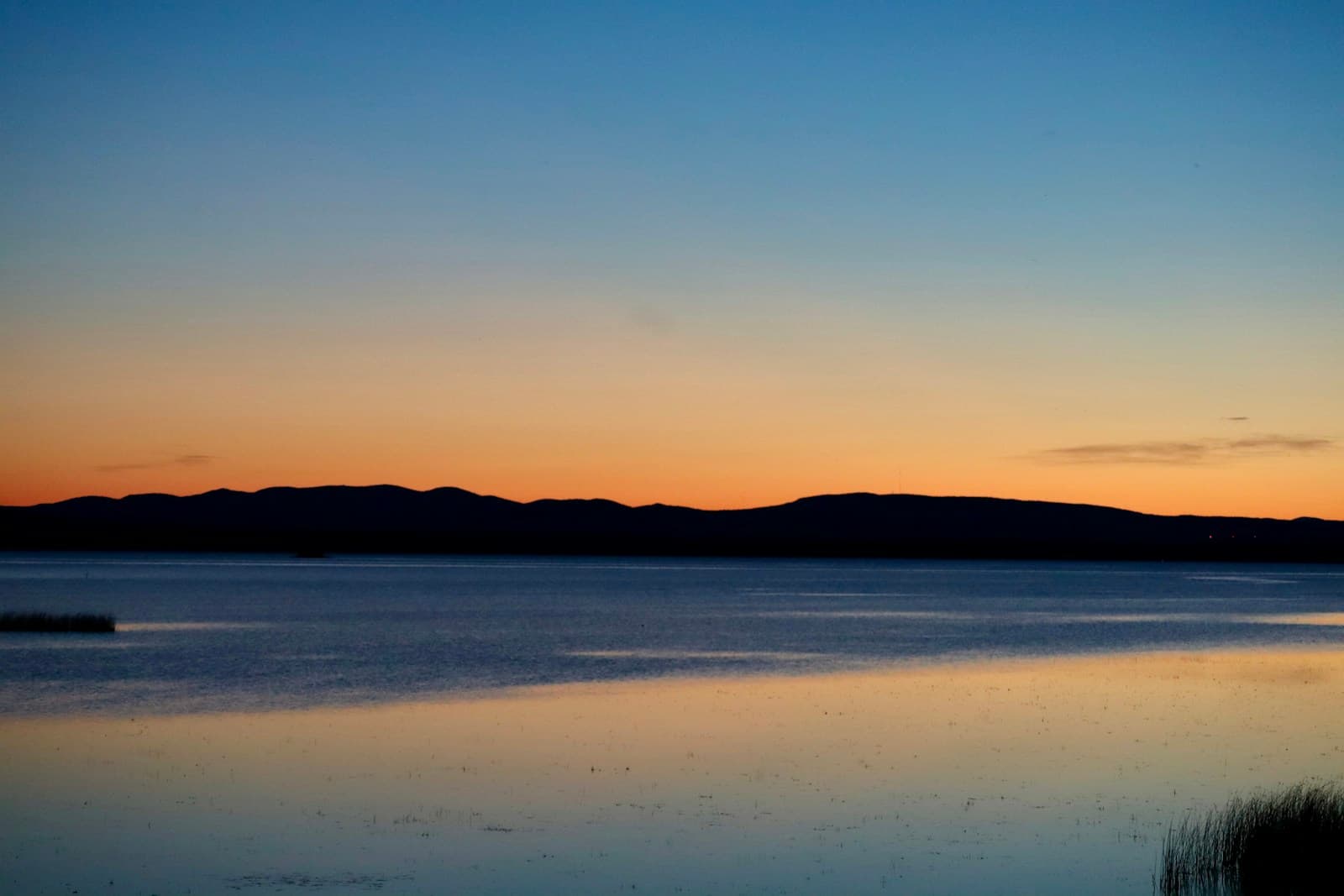 Peaceful sunset over calm lake with mountain silhouettes and golden sky reflections on water