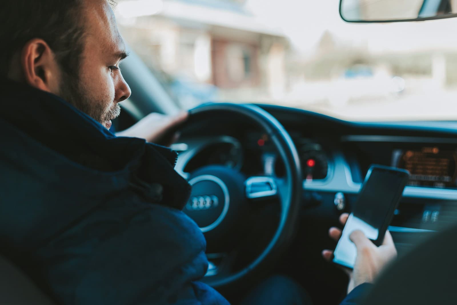 Man in the driver's seat checking a smartphone with city buildings through the windshield
