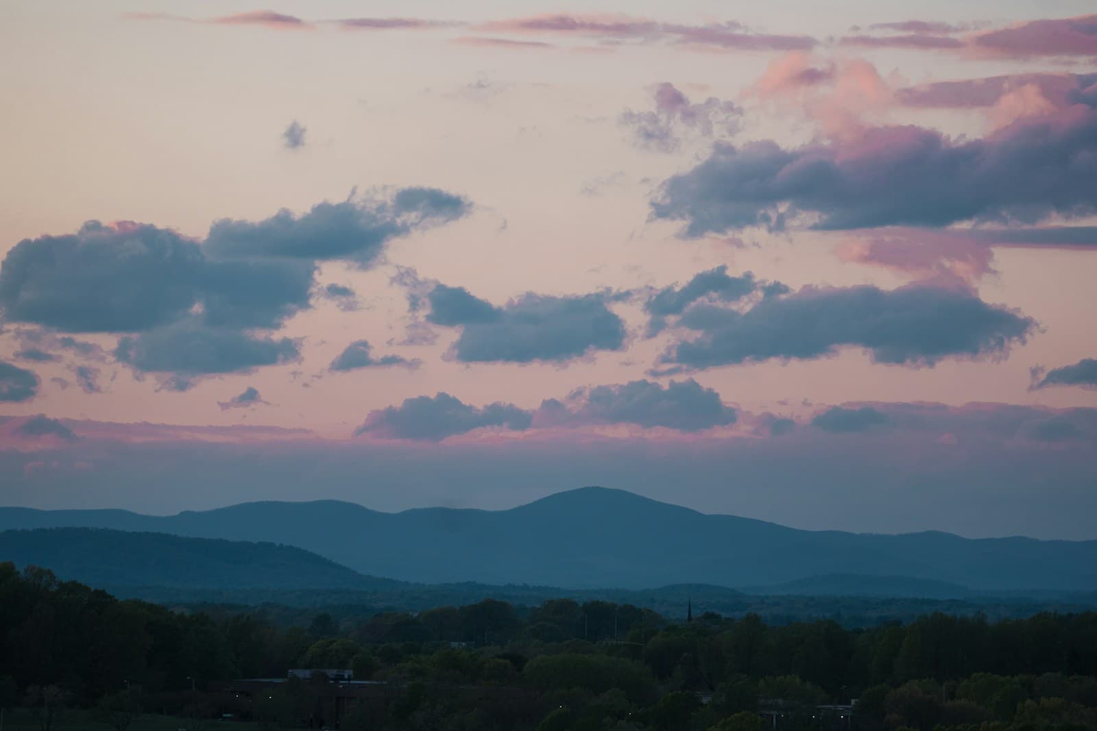 Twilight mountain landscape with pink and purple clouds over rolling hills at sunset