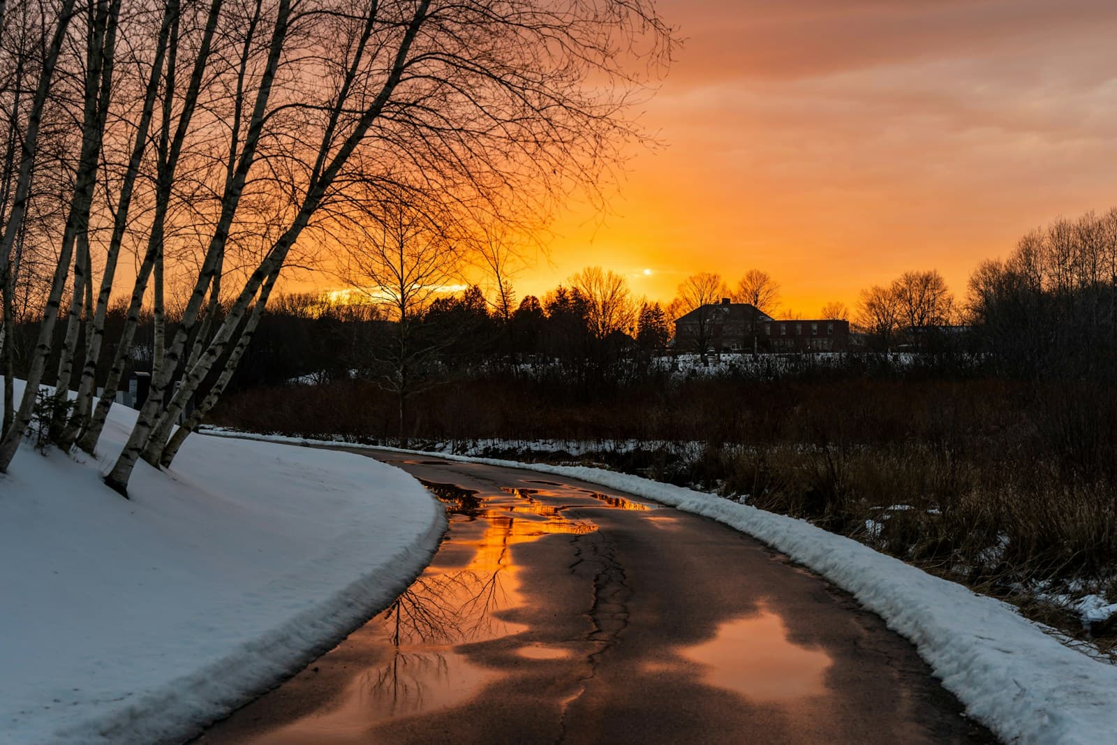 Winter creek flowing through snowy landscape at sunset with orange sky reflecting in water