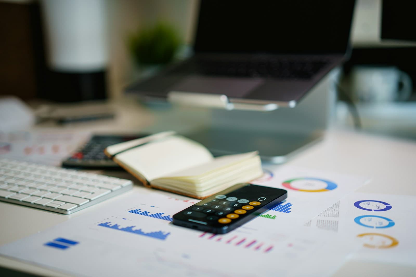 Cluttered desk with an open book, calculator, and printed charts beside a keyboard