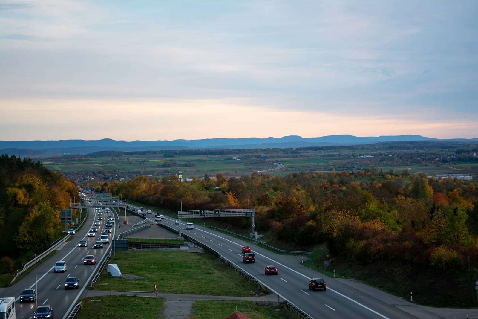 Highway with autumn trees and mountain views at dusk, cars traveling on divided road through fall landscape