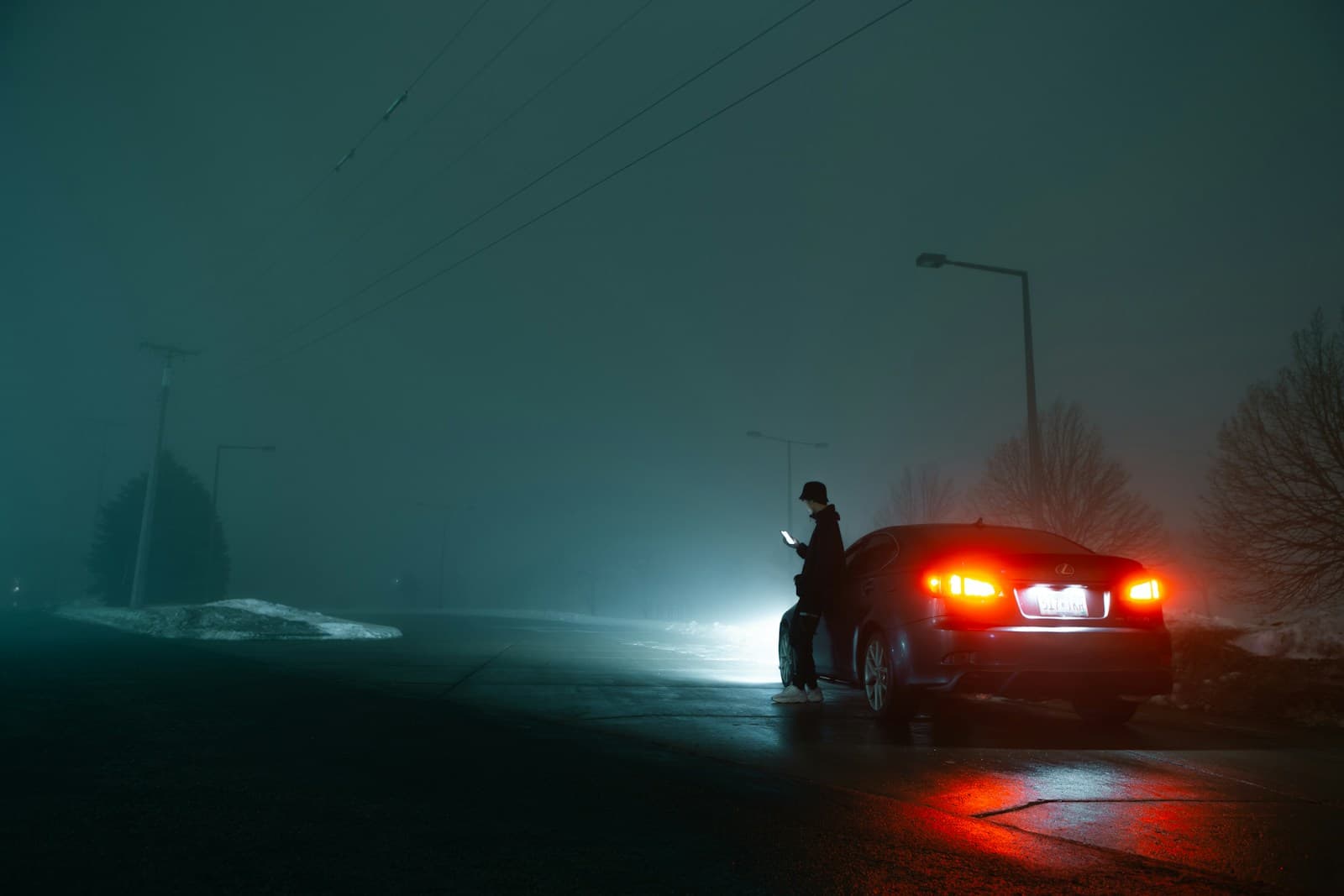 Person beside a car with glowing taillights on a foggy road at night