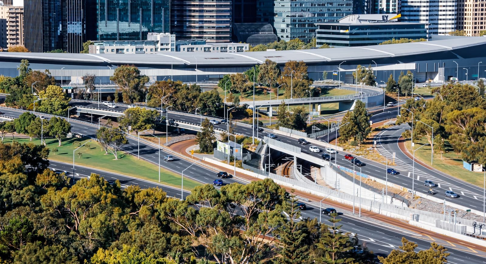 Aerial view of elevated railway tracks and transit station surrounded by trees with city buildings in background