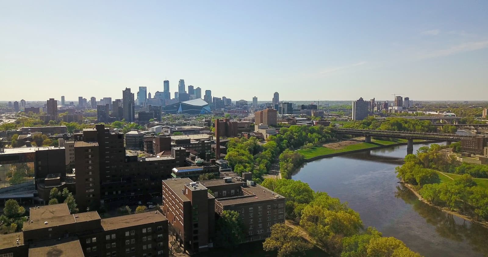 Aerial view of city skyline with downtown skyscrapers, river, and mixed residential buildings surrounded by trees
