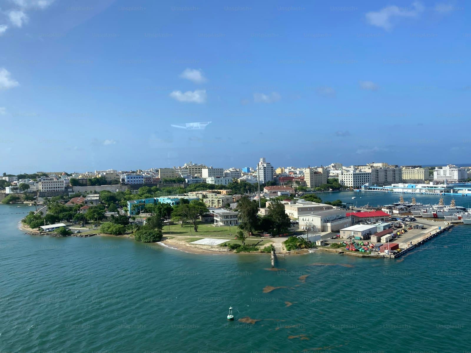 Aerial view of coastal city with turquoise water, buildings, and port infrastructure under blue sky